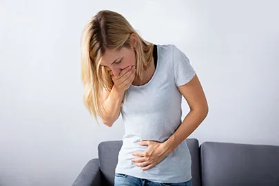 Frau hält sich mit einer Hand den Mund zu und mit der anderen den Bauch, sitzt auf einem Sofa
