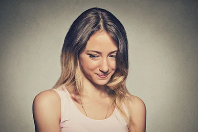 Junge Frau senkt verlegen lächelnd den Blick