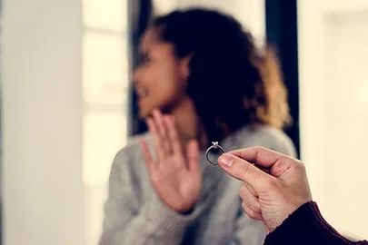 Frau wehrt mit ausgestreckter Hand einen Heiratsantrag ab, Verlobungsring im Vordergrund