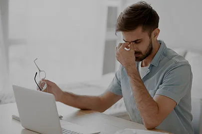 Erschöpfter Mann reibt sich die Augen am Schreibtisch vor einem Laptop
