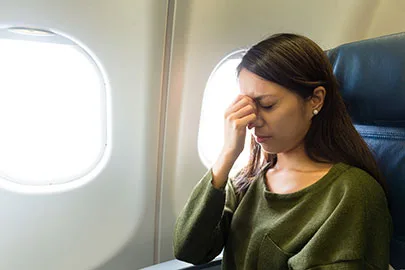 Frau im Flugzeug fasst sich angespannt an die Nasenwurzel, Fenster mit Tageslicht
