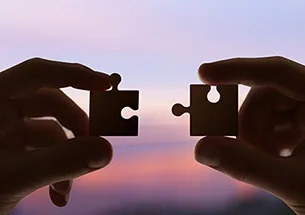 Zwei Hände halten Puzzleteile vor einem Abendhimmel, Silhouette