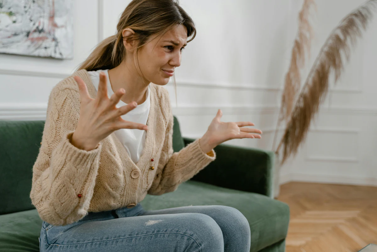 Frau sitzt auf einem Sofa und gestikuliert aufgebracht mit den Händen