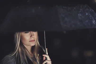 Frau steht nachdenklich unter einem Regenschirm im Dunkeln